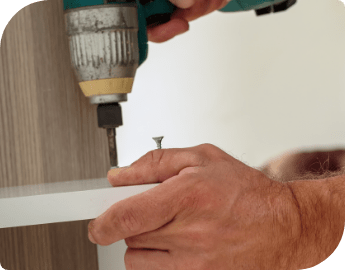 A person's hands using a tool to screw holes in a wooden furniture part