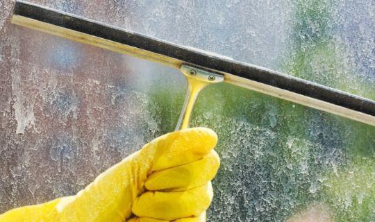 a cleaner's hand wearing a protective glove cleans limescale from a window with a squeegee