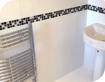 Picture of a modern bathroom with newly installed white tiles, black accents, a sink, and a towel radiator.