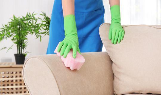 a female cleaner wearing protective gear wiping down a suede sofa with a sponge