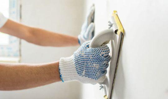 a professional wearing protective gloves applying plaster to a wall