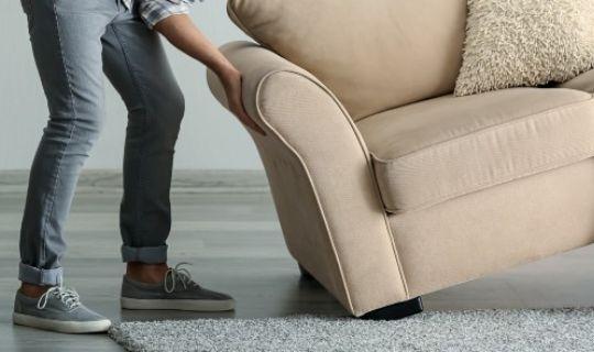 a man moving an upholstered chair on a carpet