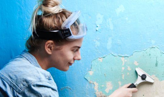 a woman removing paint from a wall by using a tool