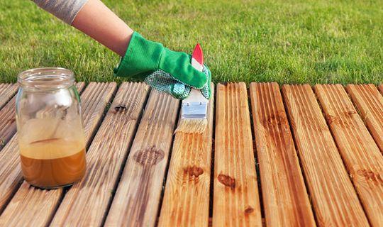 a person's hand wearing a glove staining wooden deck boards with a brush and a staining liquid