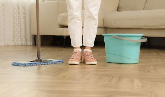 a woman's legs with white pants and a mop with a bucket next to her