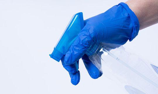 a person wearing blue protective gloves carrying a spray bottle