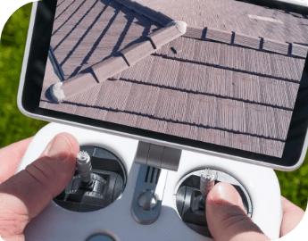 Picture of pest exterminators' hands holding a drone controller, with the screen displaying an aerial view of a roof during a bird inspection.