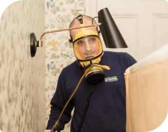 Bed bug pest control specialist wearing a dark uniform and a yellow safety mask