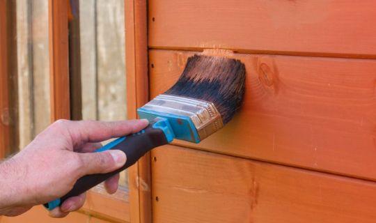 a person's hand using a brush to paint shed wooden boards in red