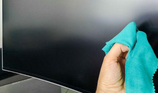 a person's hand removing fingerprints from a TV screen with a cloth