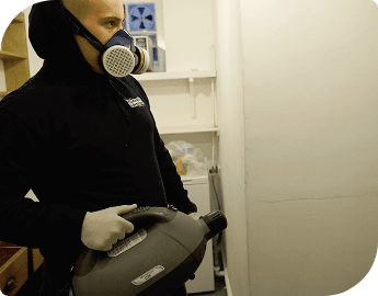 Exterminator in safety gear holding a fogging machine and preparing to conduct fogging treatment