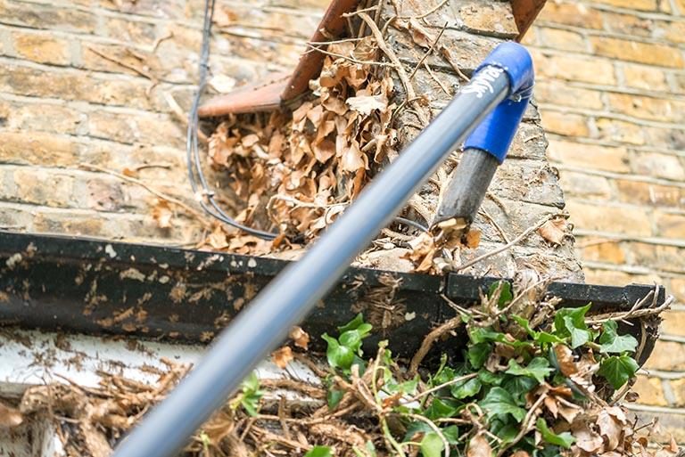 Professional gutter technician cleaning high house gutters