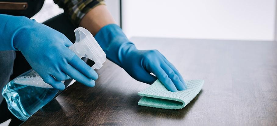 a person disinfecting a surface with a spray bottle and a cloth