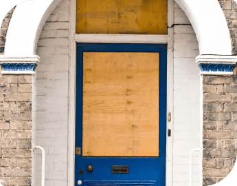 A boarded-up blue door on a brick building with an arched white frame.