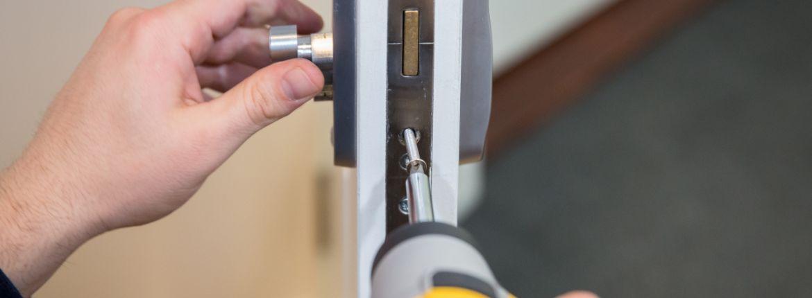 A person is fixing a door lock with a screwdriver.