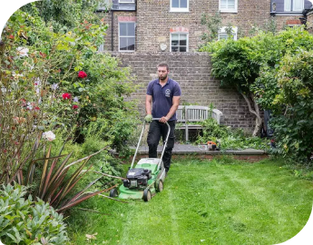 A gardener in a dark uniform mowing the lawn in a lush backyard garden.