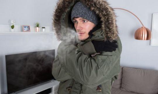 a man wearing a jacket and a winter hat being cold inside of his home