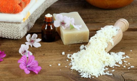 some salt, a soap, a bottle with essential oil and some beautiful pink flowers on a countertop