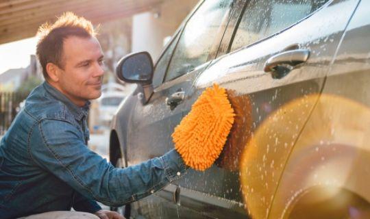 a person cleaning his car and wiping the water off with a cloth