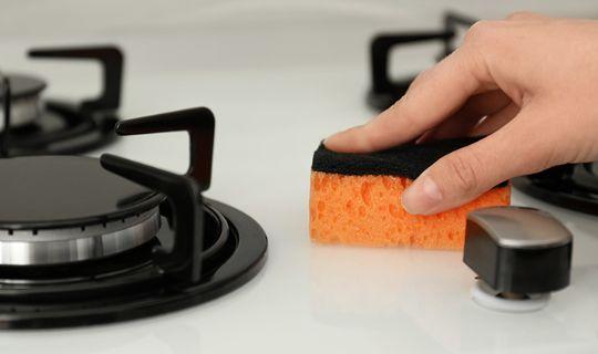 a person's hand using a sponge to clean around gas burners