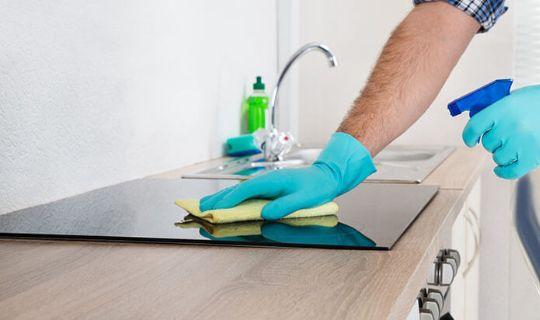 a professional using a cloth and a spray bottle to cleean an induction hob