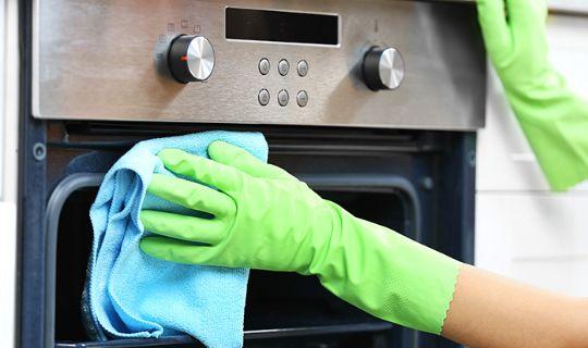 a professional cleaner's hands using a microfibre cloth wiping the front of an oven