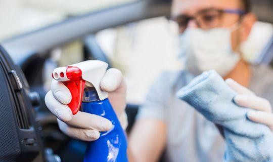 a cleaner wearing protective gear and spraying a car's interior with disinfectant solution