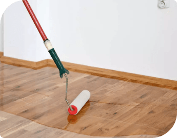 A paint roller on a handle used to apply a clear coat finish to the wood flooring.