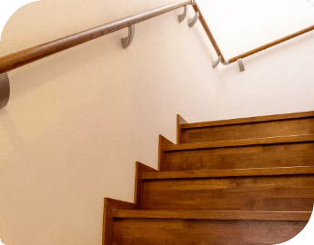 A well-sanded wooden staircase featuring handrails and a soft light illuminating the steps.