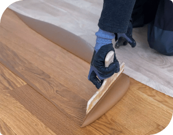 Close-up of the hand of a professional who is applying stain to wood flooring using a specialized tool.