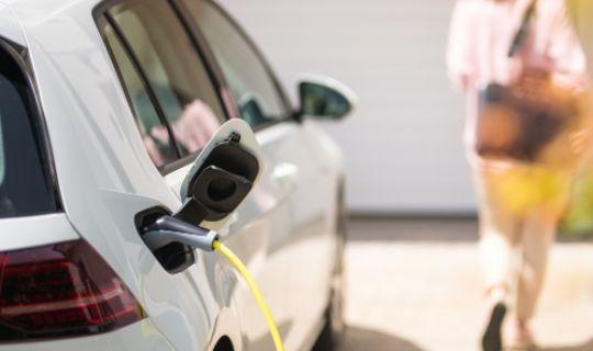 a white electric car being charged and a woman in the background