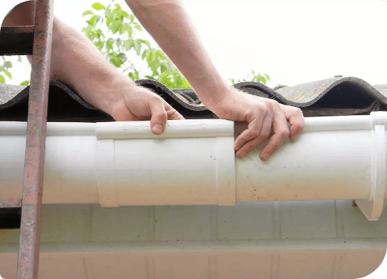 Picture of the hands of a gutter technician who repairs a white gutter on a house's roof edge.