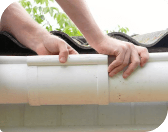 Picture of the hands of a gutter technician who repairs a white gutter on a house's roof edge.