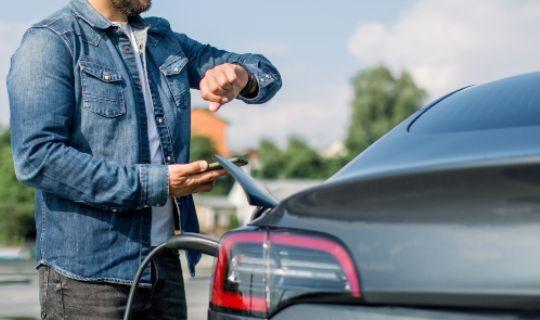 a man checking his wristwatch and waiting for his electrical vehicle to get charged