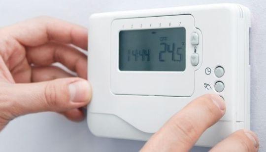 a man's hands adjusting the settings on a digital thermostat