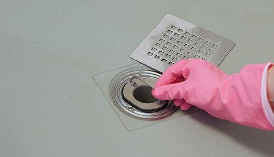 a hand with a yellow glove working on unblocking a shower drain