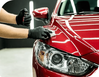 Close-up of the hands of a professional who is detailing a red car's headlight.