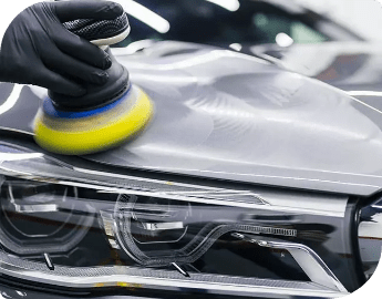 A hand in a black glove polishing a car headlight