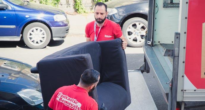 Two professional removalists moving packed furniture down the stairs of a property.