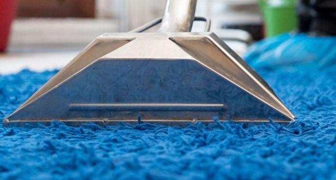 A carpet cleaning technician who is wearing a dark blue Fantastic Services uniform and using a hot water extraction machine to deep clean a wall-to-wall carpet.