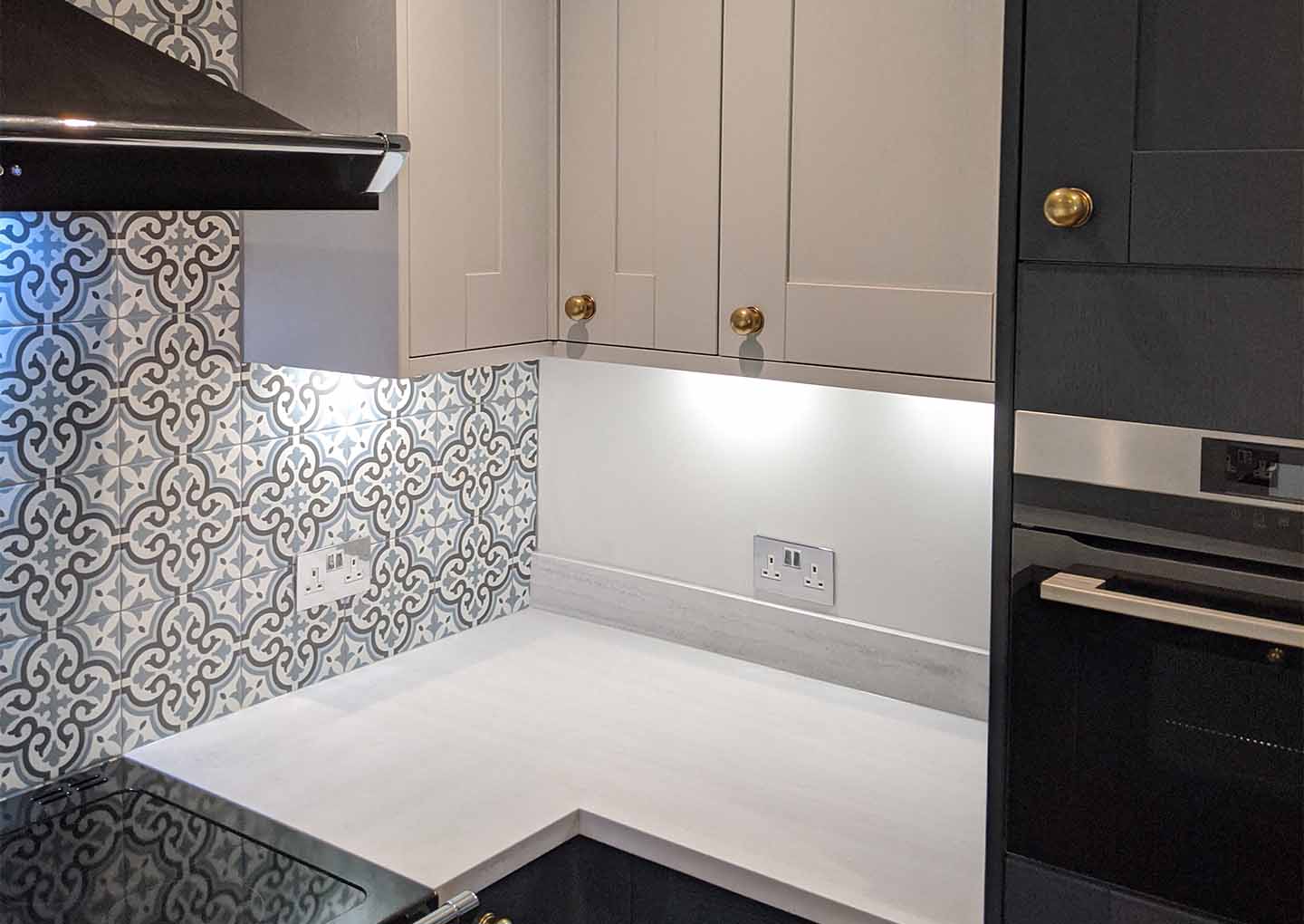 Modern kitchen corner with patterned backsplash, beige cabinets, black oven, and extractor hood.