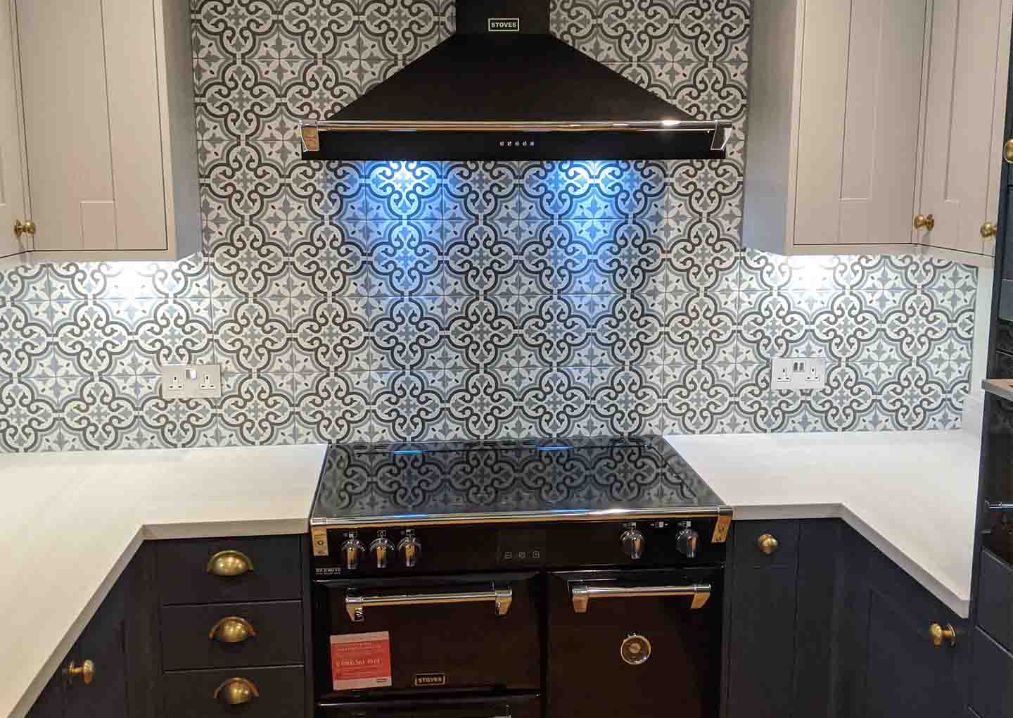 Modern stove and range hood with ornate backsplash in a kitchen.