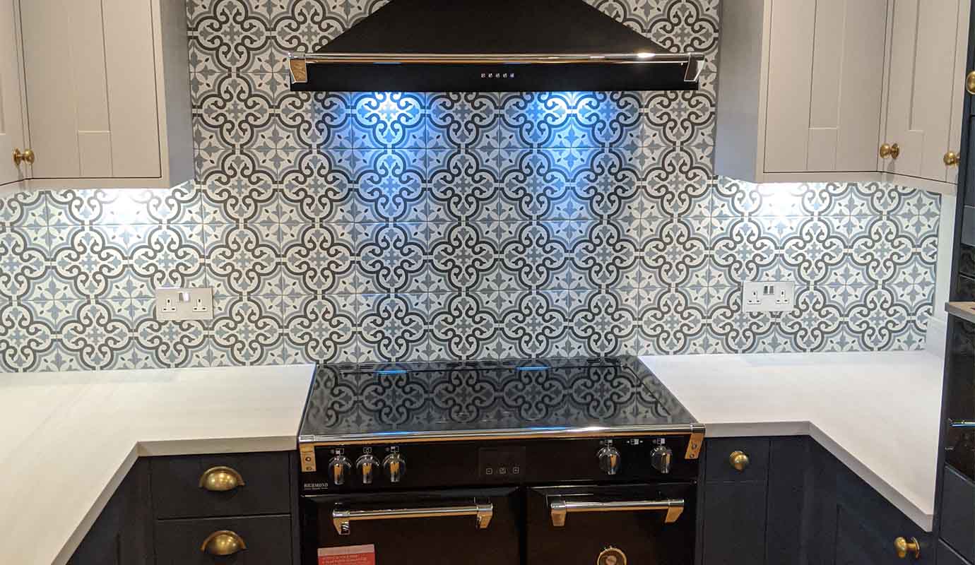 Modern stove and range hood with ornate backsplash in a kitchen.
