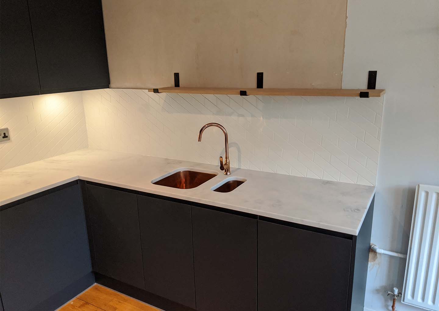 Modern kitchen with dark cabinets, white herringbone backsplash, and copper faucet.