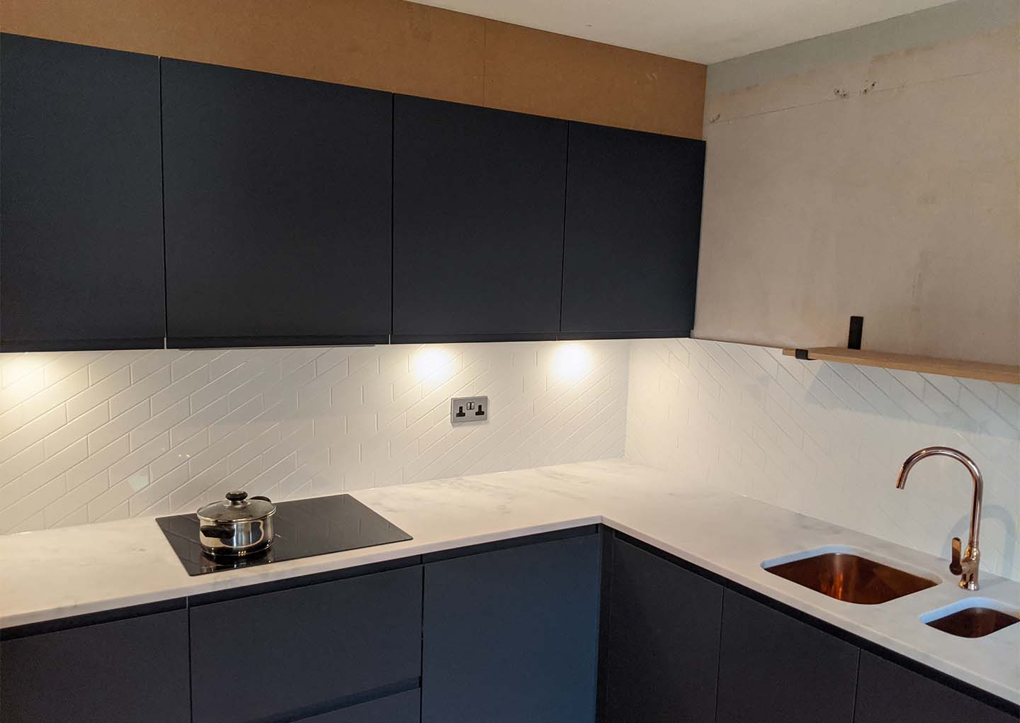 Modern kitchen with dark cabinetry, white herringbone backsplash, and copper sink.