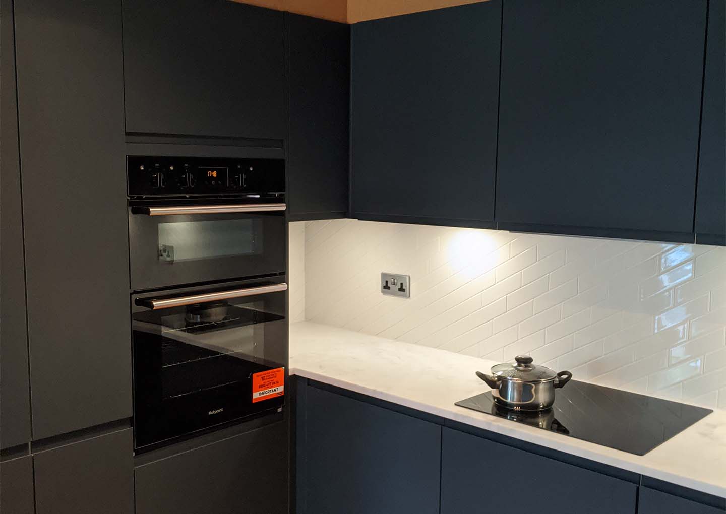 Modern kitchen with dark cabinetry, built-in ovens, and a pot on a cooktop.