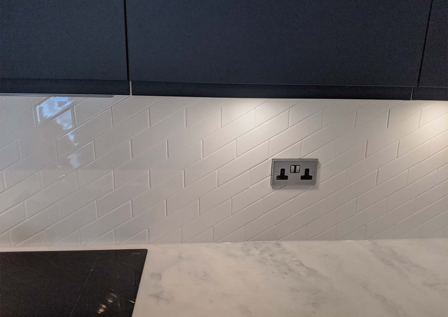 A modern kitchen with herringbone tile backsplash, marble countertop, and a UK style power socket.