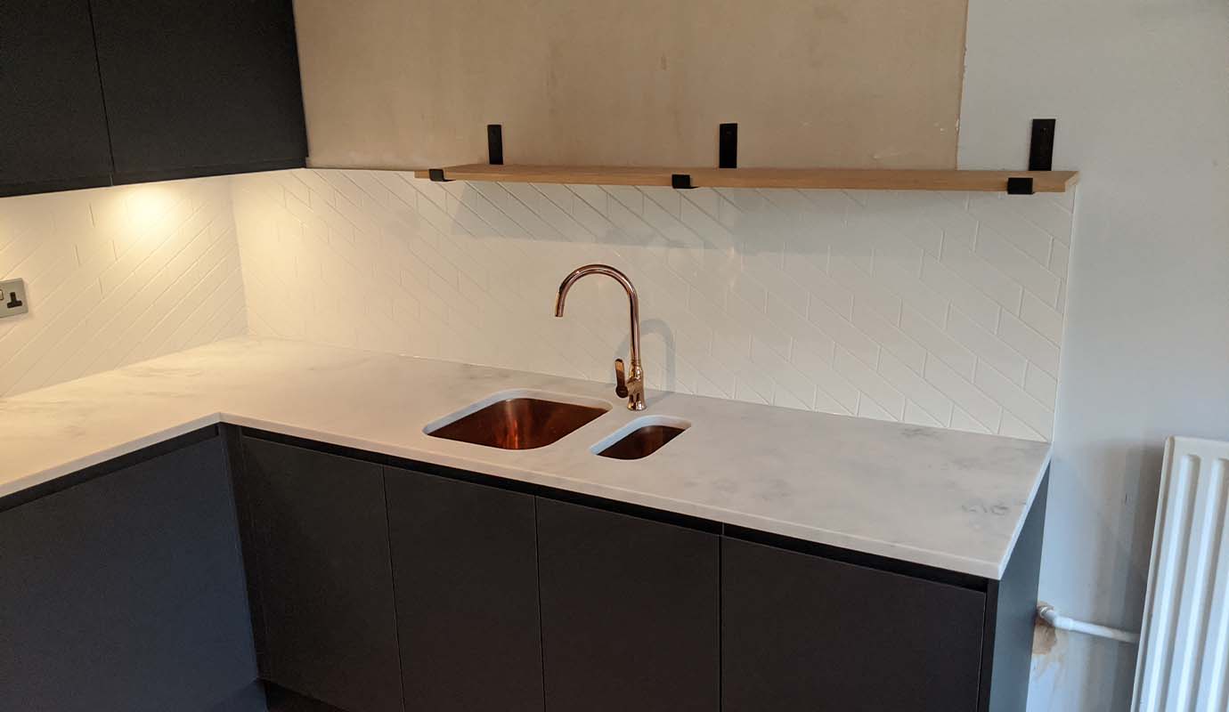 Modern kitchen with dark cabinets, white herringbone backsplash, and copper faucet.