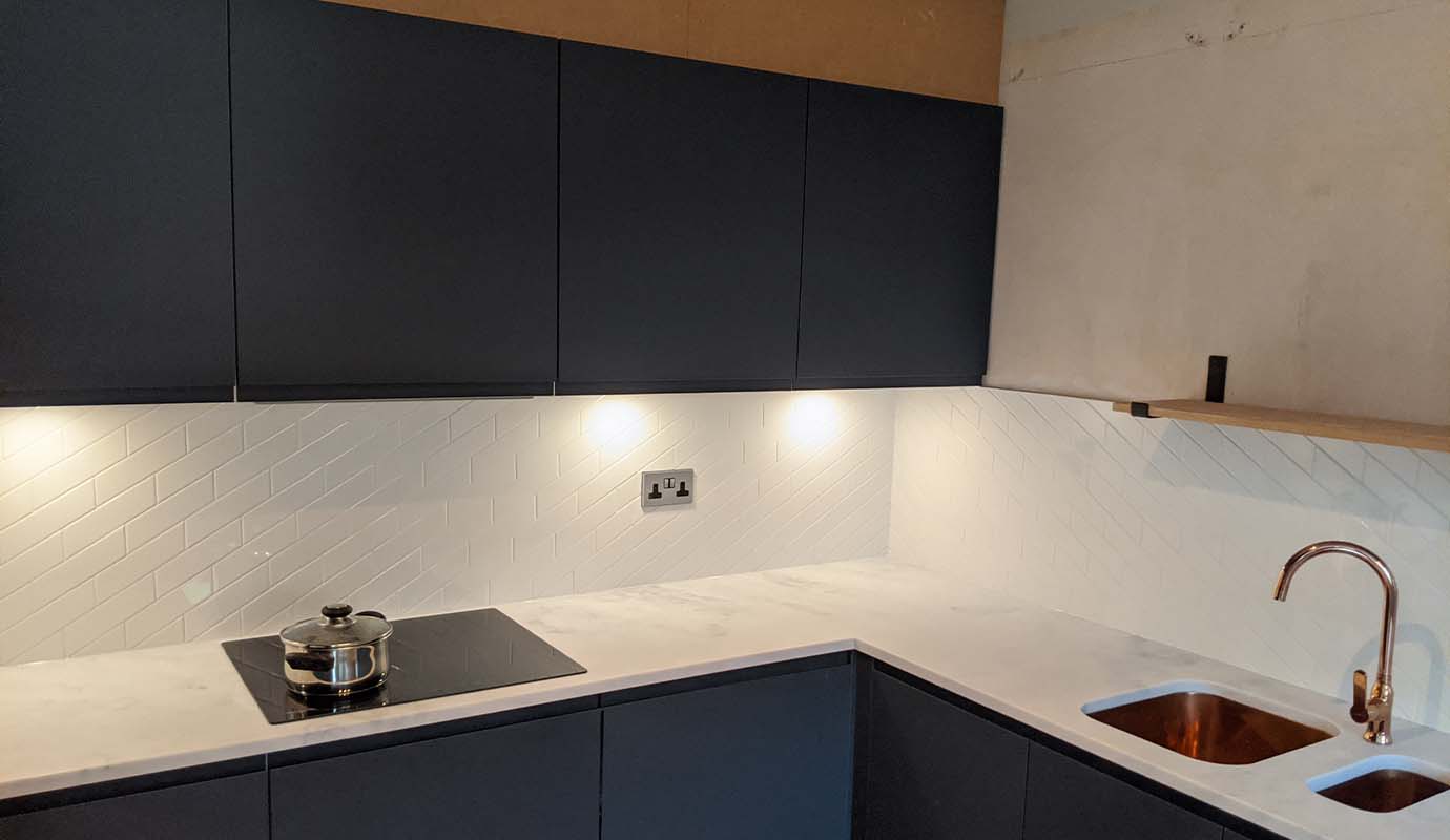 Modern kitchen with dark cabinetry, white herringbone backsplash, and copper sink.