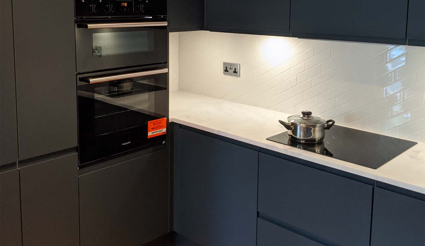 Modern kitchen with dark cabinetry, built-in ovens, and a pot on a cooktop.